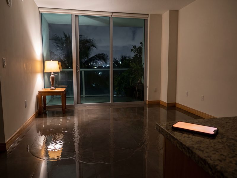 Water spreading across a tiled condominium floor at night, lit by a single lamp and a phone screen.
