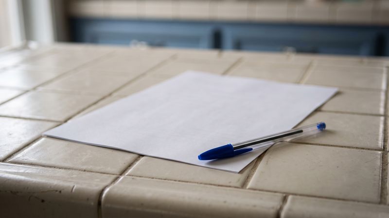 A single blank sheet of paper with a blue ballpoint pen lying across its lower edge on a tiled counter