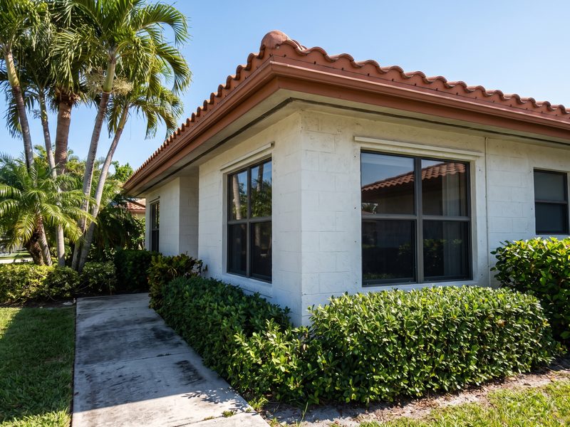 Exterior corner of a white stucco concrete-block house in South Florida with a barrel-tile roof edge.