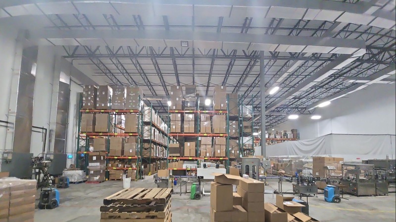 Portable dehumidifiers running on a bare concrete warehouse floor beside loaded pallet racking