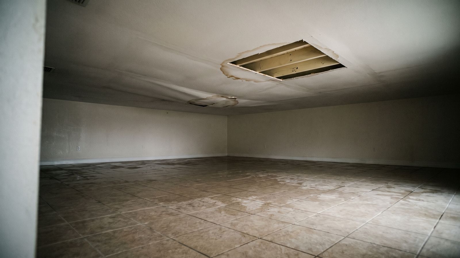 Stained ceiling cut open above a wet tile floor Water-stained drywall ceiling opened over exposed joists above a wet tile floor after hurricane water damage