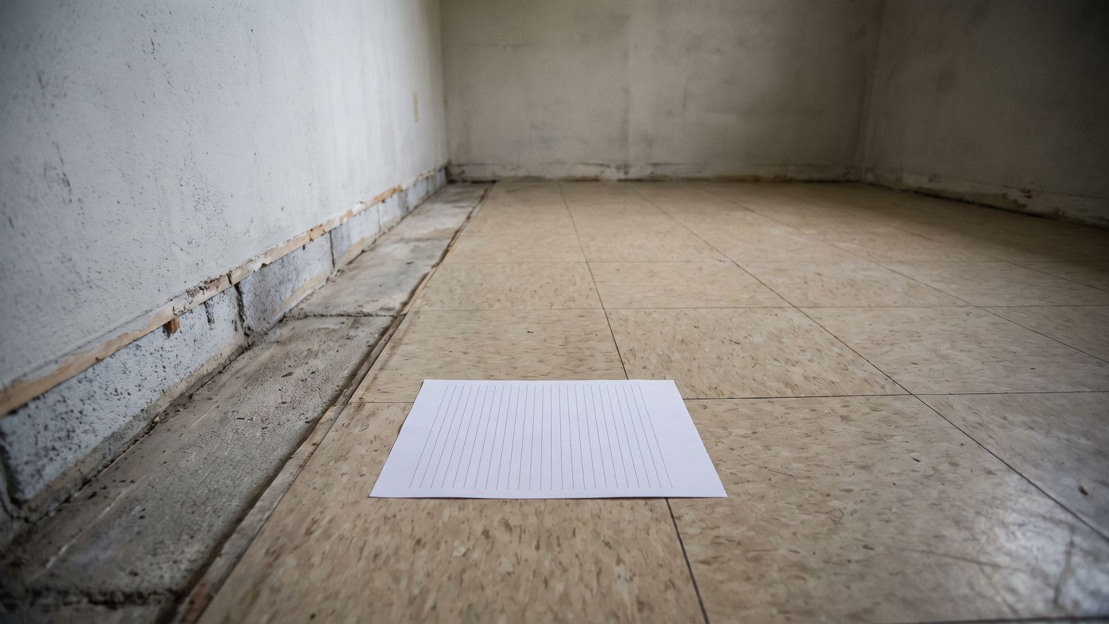 A Ruled Page Beside an Opened Wall A sheet of evenly ruled paper lying flat on a tile floor beside a wall where the baseboard has been pried away.