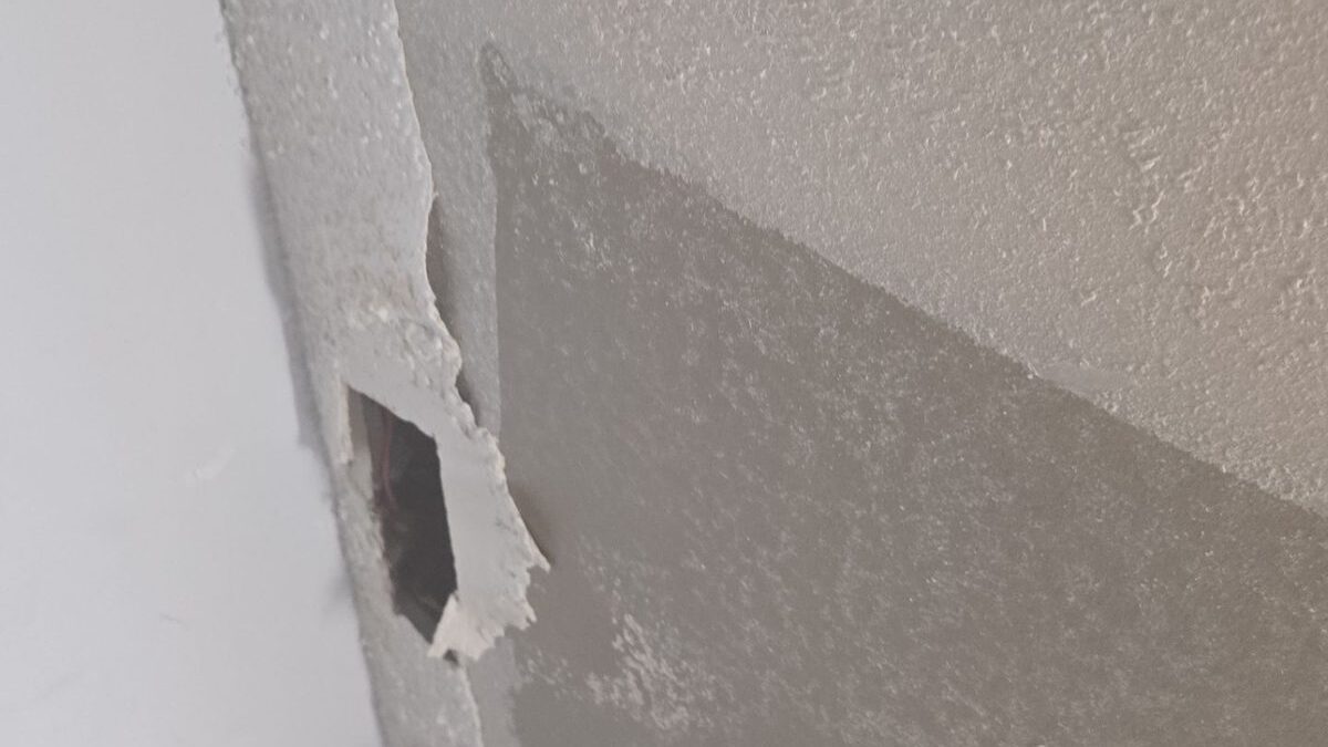 Torn ceiling texture and a punched hole exposing wiring above a broken drywall edge
