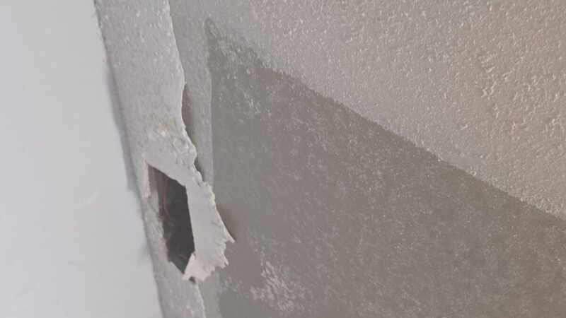 Torn ceiling texture and a punched hole exposing wiring above a broken drywall edge