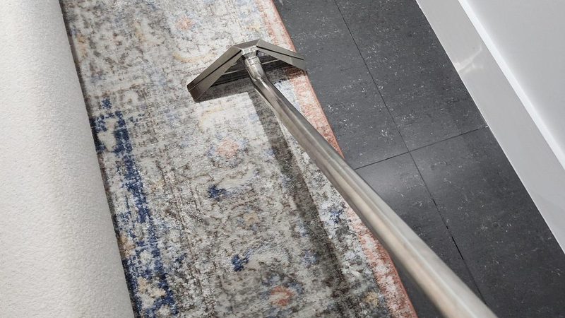 An extraction wand drawing water from a runner rug laid beside dark tile flooring