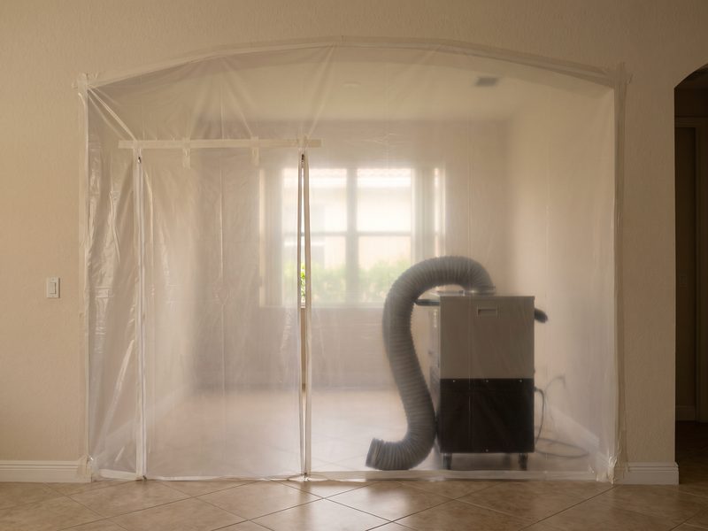 Clear polyethylene containment with a zippered entry inside a Coral Gables home, air scrubber behind it.