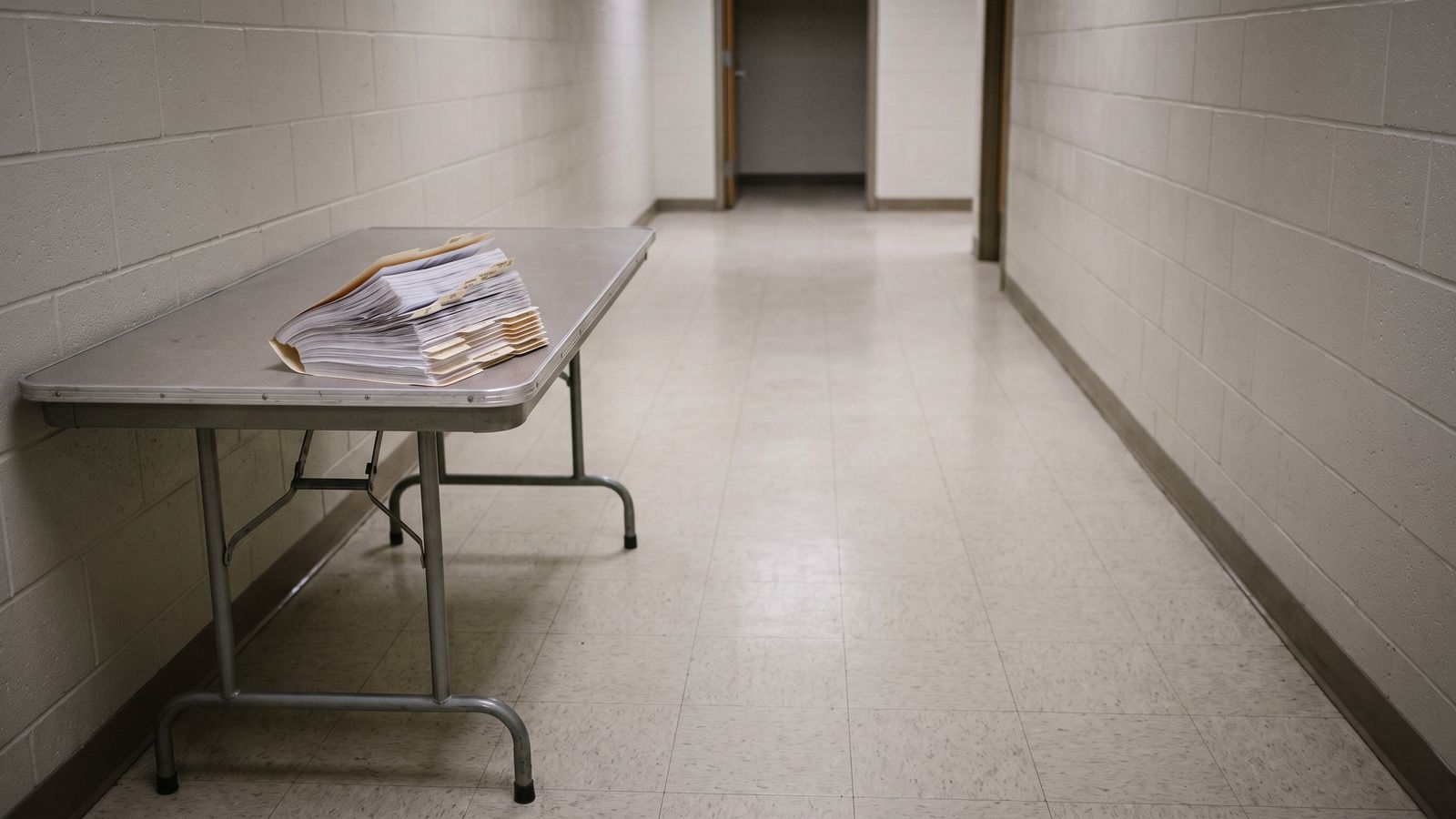 A Document Set on a Folding Table A thick fanned document set with folder tabs resting on a metal folding table in a painted block corridor.