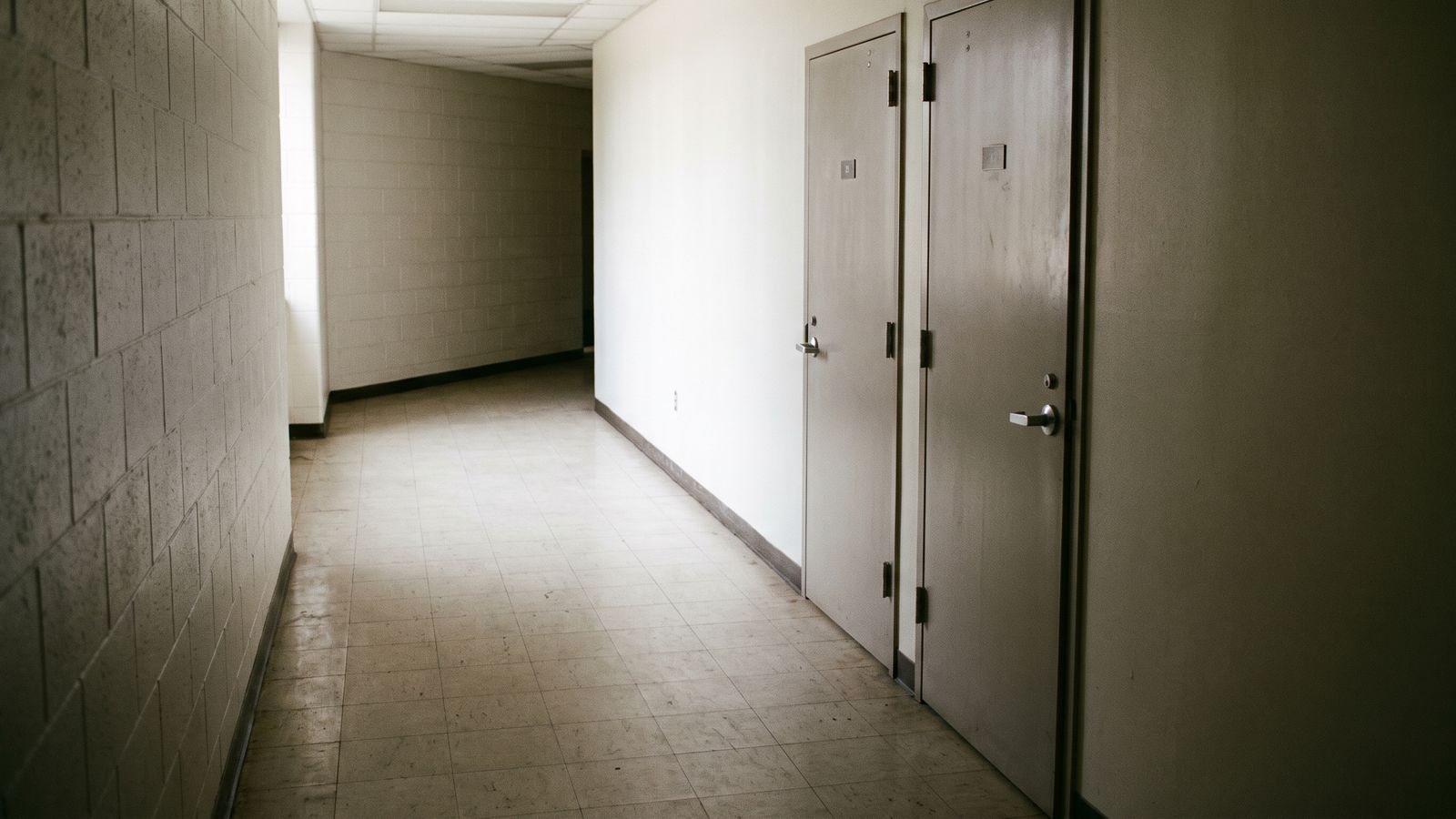 Two Unit Doors on a Bare Corridor Two closed unit doors along a bare tiled corridor, with the numeral plates too small to read.