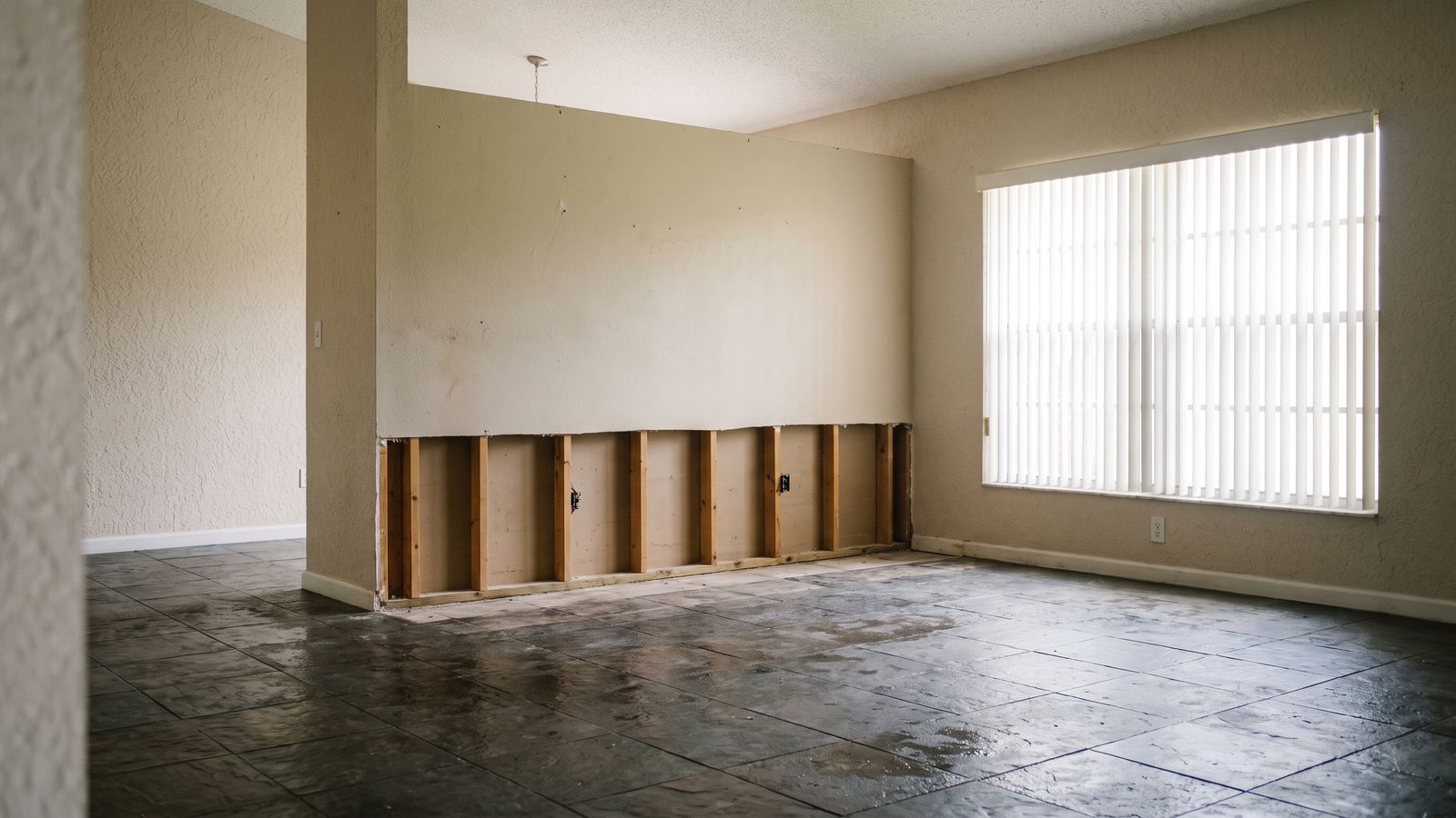 Flood-cut drywall, bare studs and a wet tile floor in an emptied South Florida room, the scope a restoration deposit funds.