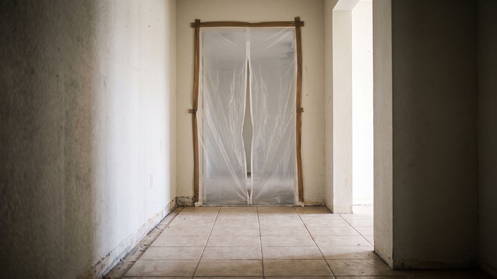 Containment Sheeting Sealed Doorway | Restoration Doctor Containment sheeting taped floor to ceiling across a tiled hallway doorway, baseboard removed, in a sewer backup cleanup.