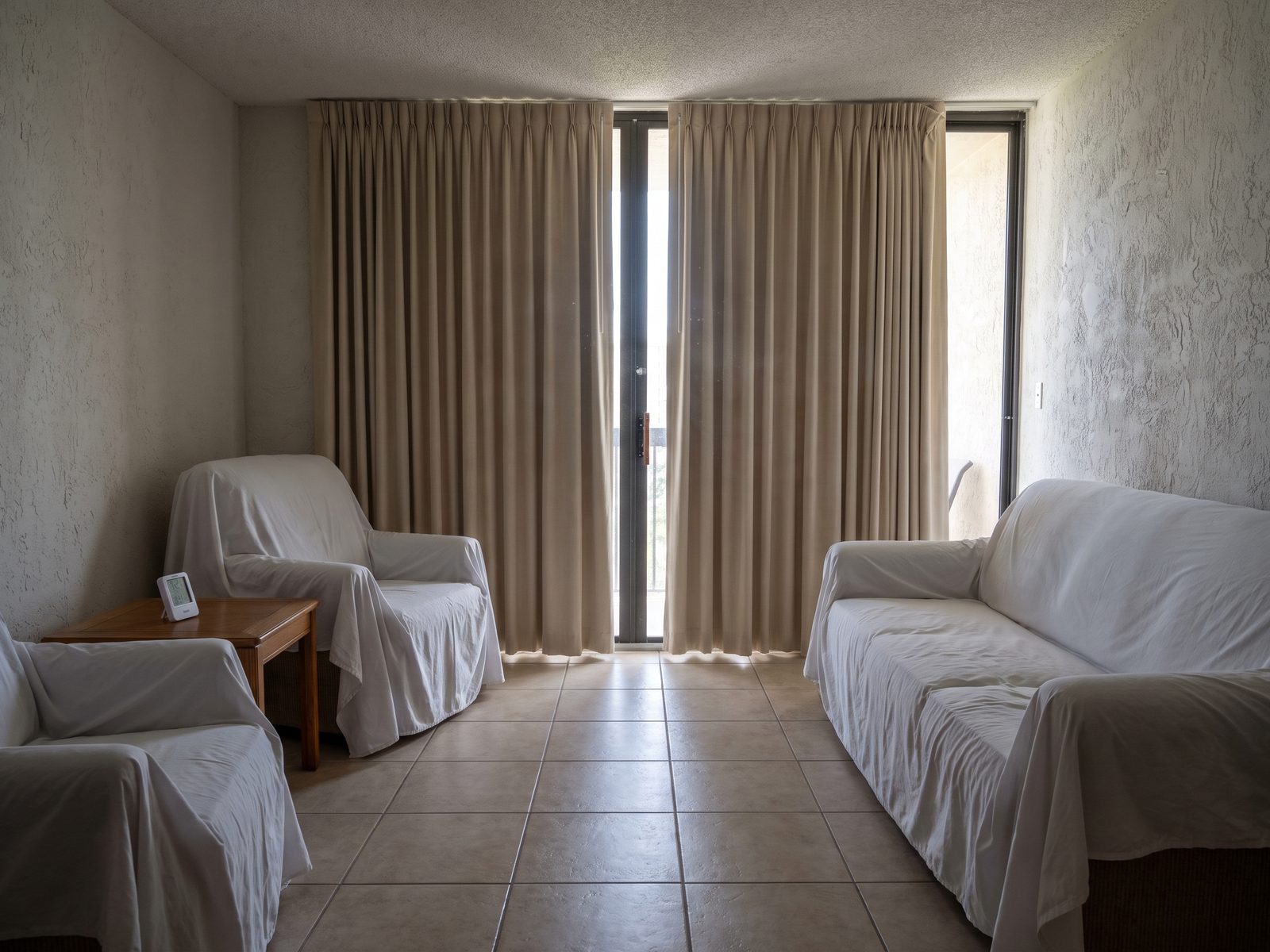Closed-up seasonal condominium interior with furniture under dust sheets and a hygrometer on a side table.