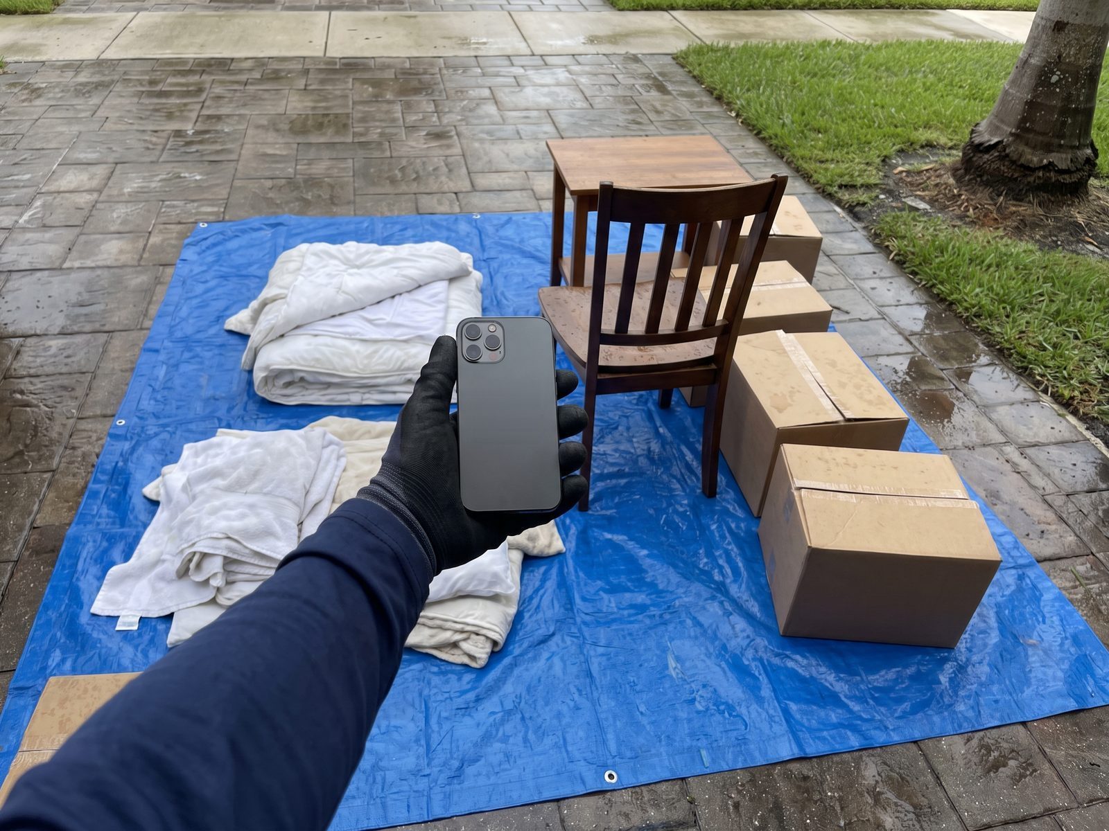 A gloved technician holding a phone over household contents laid out on a tarp before they are moved.
