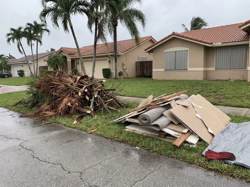 Separated vegetative and building-material debris piles at the swale of a South Florida street after a storm.