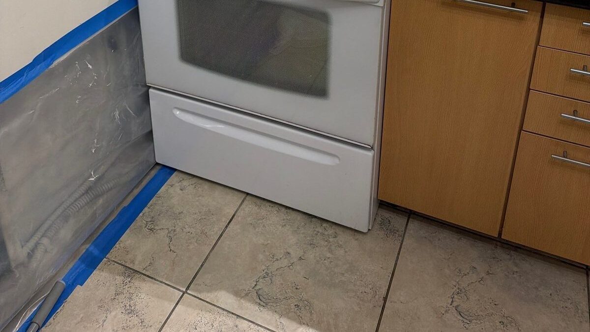 Plastic sheeting taped along a kitchen wall beside an oven front and tiled floor