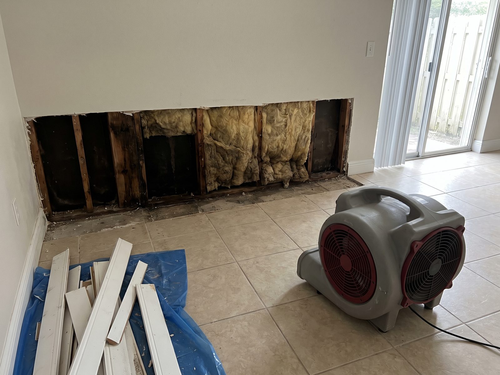 Opened Wall Cavity Florida | Restoration Doctor Low section of drywall removed along an interior wall, exposing damp framing and wet insulation above a tile floor.