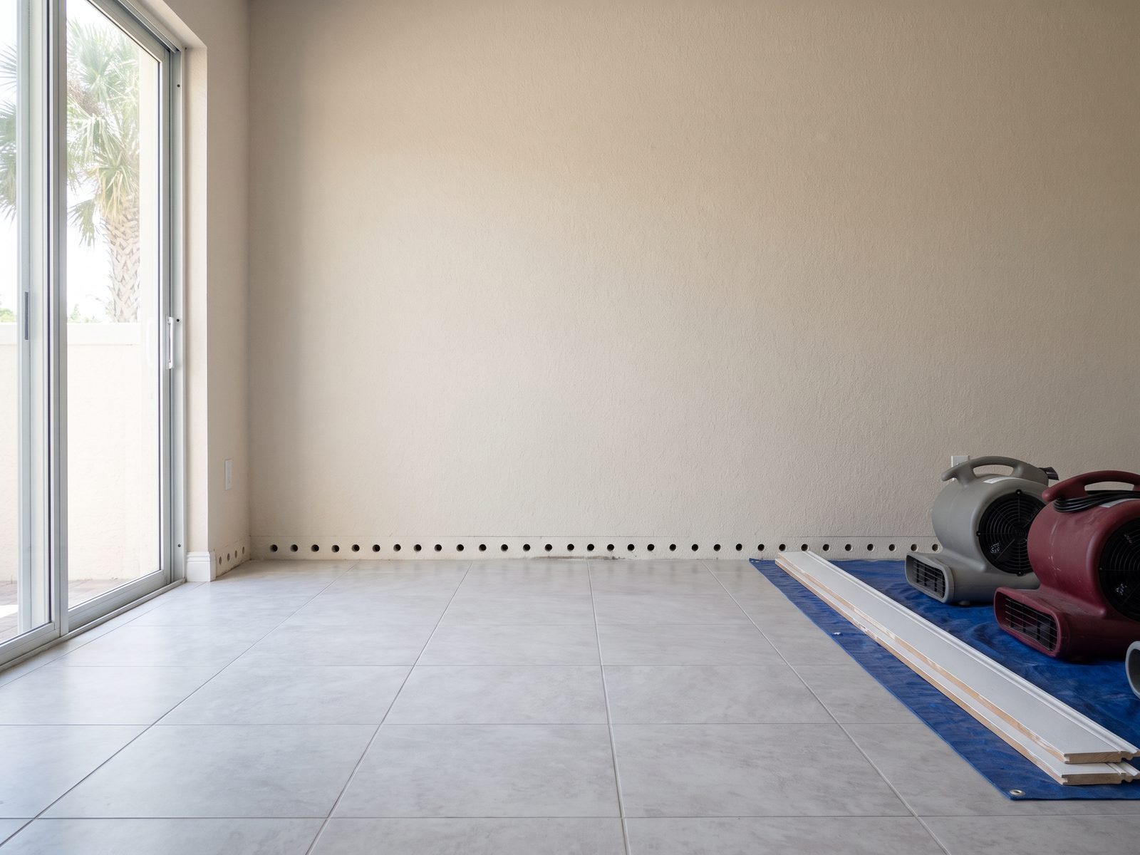 Row of small drilled holes along a wall above a tile floor with the baseboard removed and set aside.