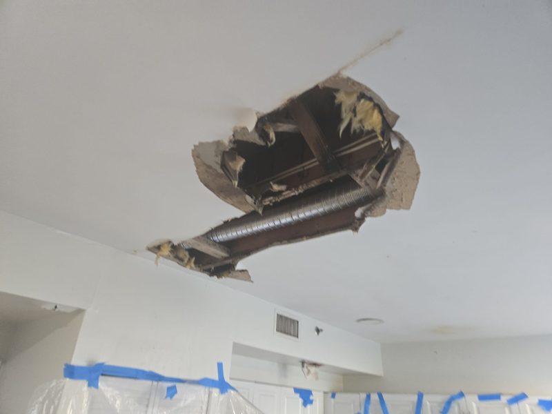 A ceiling opened to the joists with a flexible duct and insulation exposed, and plastic sheeting taped up below, in a Miami Beach, FL unit, January 2026, Restoration Doctor project documentation.
