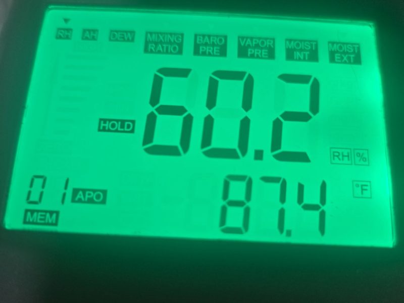 A handheld humidity meter display in a Miami Beach, FL unit on January 7, 2026, set to relative humidity with HOLD shown, reading 60.2 percent and 87.4 degrees Fahrenheit, Restoration Doctor project documentation.