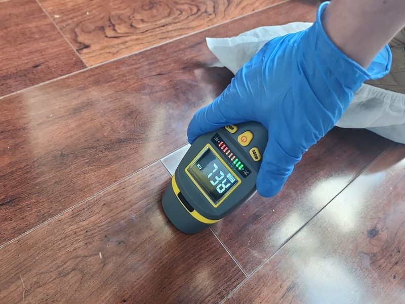 Gloved hand holding a pinless moisture meter flat against a wood-look plank floor in Kendall, FL, October 2024, Restoration Doctor project documentation.